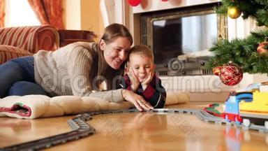 快乐微笑的家庭躺在客厅的地板上，看着骑玩具火车的4k视频。 儿童接受礼物